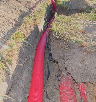 Cables in the trench. High voltage cables in protective red cover in the trench. Concept of electrical installations, construction works, building renovations and building refurbishments.