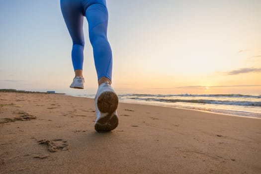 legs of a girl in blue leggings and sneakers running along the beach at dawn with space for inscription. High quality photo