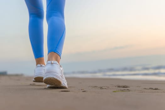 legs of a girl in blue leggings and sneakers running along the beach with space for inscription. High quality photo