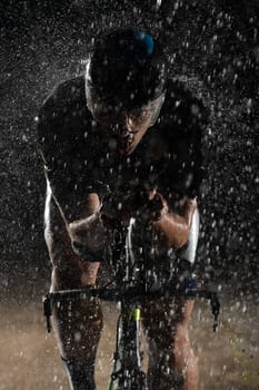 A triathlete braving the rain as he cycles through the night, preparing himself for the upcoming marathon. The blurred raindrops in the foreground and the dark, moody atmosphere in the background add to the sense of determination and grit shown by the athlete