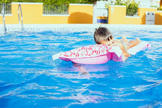 Happy boy resting on a pink inflatable mattress in the pool, there is a place for an inscription. High quality photo
