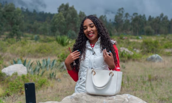 vlogger from ecuador doing a hairstyle and makeup tutorial for her followers in the mountains of ecuador with a white bag on a big rock. High quality photo
