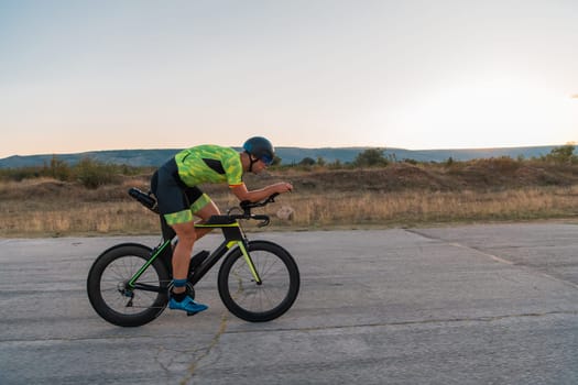 Triathlete riding his bicycle during sunset, preparing for a marathon. The warm colors of the sky provide a beautiful backdrop for his determined and focused effort