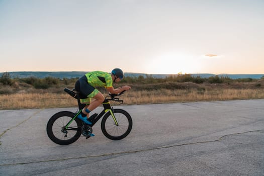 Triathlete riding his bicycle during sunset, preparing for a marathon. The warm colors of the sky provide a beautiful backdrop for his determined and focused effort