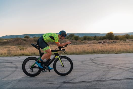 Triathlete riding his bicycle during sunset, preparing for a marathon. The warm colors of the sky provide a beautiful backdrop for his determined and focused effort