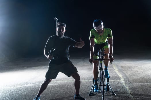 Behind the scenes. Professional videographer on a night shoot with a triathlete riding a bicycle for video recording purposes.