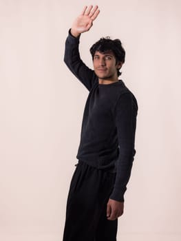 A man in a black shirt and black pants greeting with one hand, saluting raising his hand, in studio shot