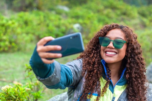 pretty latina and tourism vlogger with green glasses and curly hair showing her followers the mountain place where she is. High quality photo