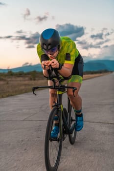 Triathlete riding his bicycle during sunset, preparing for a marathon. The warm colors of the sky provide a beautiful backdrop for his determined and focused effort