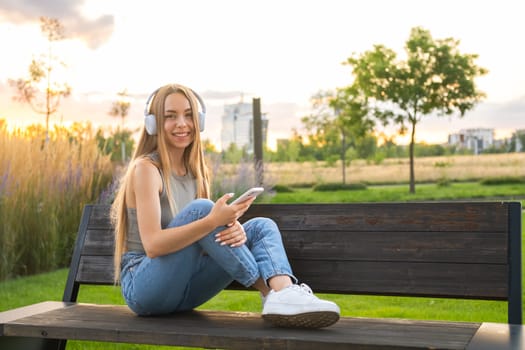 Freelancer enjoys music via headphones sitting on the bench in the park.