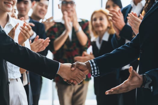 Cropped image of businessmen shaking hand and making a contract in the sign of agreement, cooperation rounded with smiling employees clapping hands and applause behind. Front view. Intellectual.