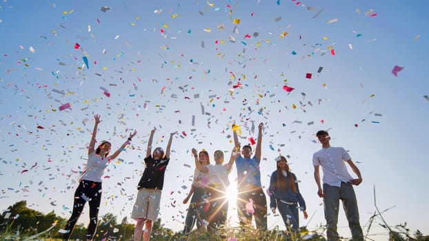 Friends toss colorful paper confetti from their hands against the rays of the evening sun