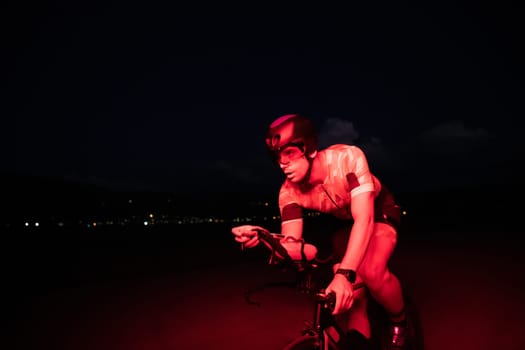 A triathlete rides his bike in the darkness of night, pushing himself to prepare for a marathon. The contrast between the darkness and the light of his bike creates a sense of drama and highlights the athlete's determination and perseverance