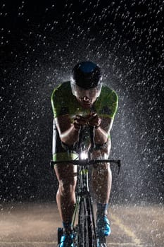 A triathlete braving the rain as he cycles through the night, preparing himself for the upcoming marathon. The blurred raindrops in the foreground and the dark, moody atmosphere in the background add to the sense of determination and grit shown by the athlete