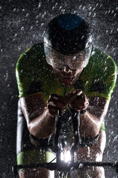 A triathlete braving the rain as he cycles through the night, preparing himself for the upcoming marathon. The blurred raindrops in the foreground and the dark, moody atmosphere in the background add to the sense of determination and grit shown by the athlete