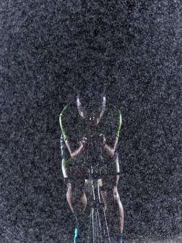 A triathlete braving the rain as he cycles through the night, preparing himself for the upcoming marathon. The blurred raindrops in the foreground and the dark, moody atmosphere in the background add to the sense of determination and grit shown by the athlete