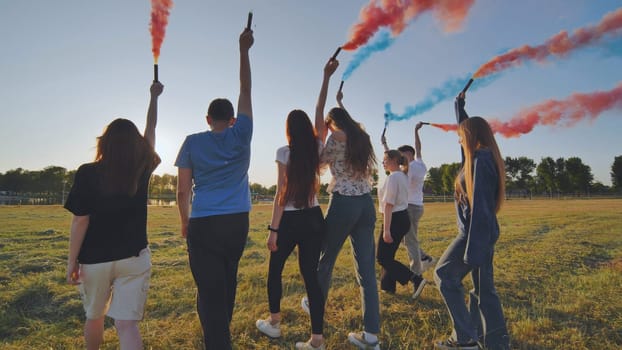 A group of friends spraying multi-colored smoke at sunset