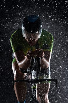 A triathlete braving the rain as he cycles through the night, preparing himself for the upcoming marathon. The blurred raindrops in the foreground and the dark, moody atmosphere in the background add to the sense of determination and grit shown by the athlete