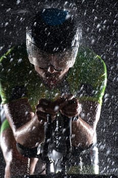 A triathlete braving the rain as he cycles through the night, preparing himself for the upcoming marathon. The blurred raindrops in the foreground and the dark, moody atmosphere in the background add to the sense of determination and grit shown by the athlete