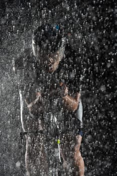 A triathlete braving the rain as he cycles through the night, preparing himself for the upcoming marathon. The blurred raindrops in the foreground and the dark, moody atmosphere in the background add to the sense of determination and grit shown by the athlete