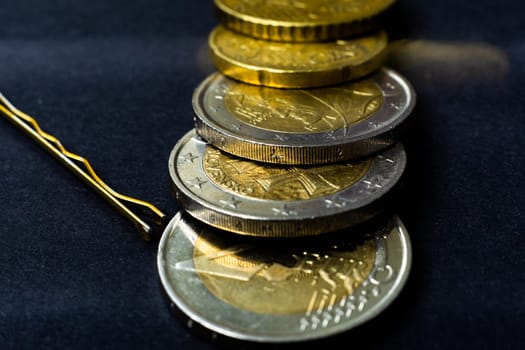 Money concept. Hairpin with coins euro, close up, dark black background