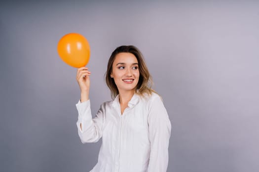 Close up portrait of young woman inflating balloon on isolated grey background