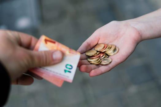 Close-up of hand giving coins to another hand with banknotes