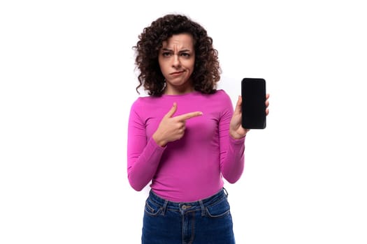 young fashionista curly brunette lady dressed in a fresh lilac color turtleneck points her finger at a smartphone.