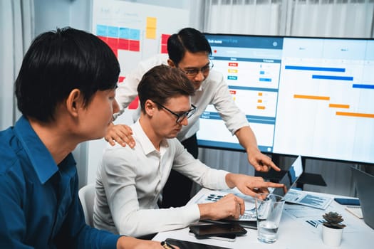 Project manager communicate and collaborate with team using project management software display on monitor, tracking progress of project task and making schedule plan at meeting table. Prudent