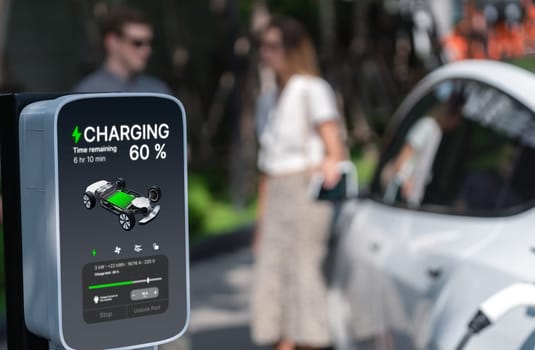 Young couple travel with EV electric car charging in green sustainable city outdoor garden in summer shows urban sustainability lifestyle by green clean rechargeable energy of electric vehicle innards