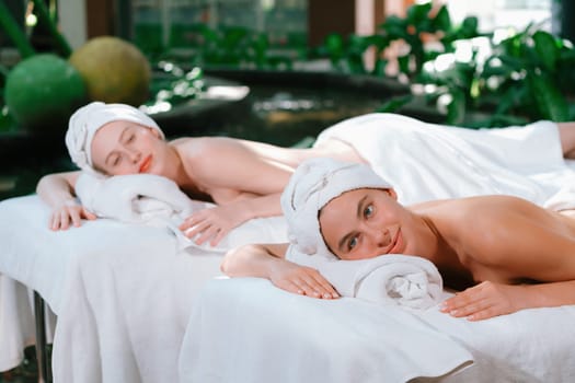 A portrait of a couple of a beautiful young caucasian woman with white towel rest on comfortable spa bed with relaxation while having body massage with professional masseur at spa salon.Tranquility.