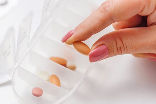 Woman hand taking pill from pillbox or organizer for daily medication. Health care and diseases cure