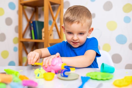 Little boy enthusiastically plays with plasticine, play dough on white table at home, children's creativity concept. Development of fine motor skills