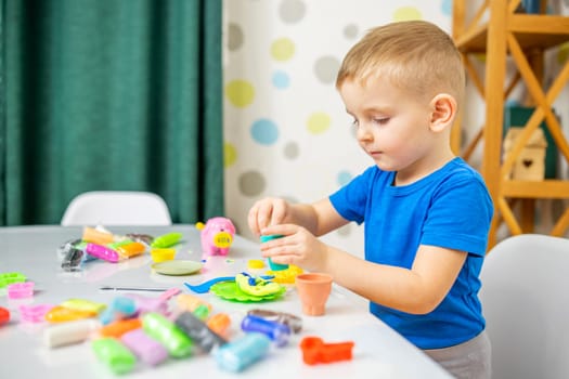 Little boy enthusiastically plays with plasticine, play dough on white table at home, children's creativity concept. Development of fine motor skills