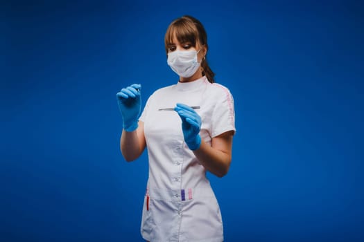 An attractive young female doctor holds a scalpel and looks directly at the camera. Concept of healthcare, treatment and surgery. Portrait of a medical practitioner on a blue background.