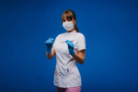 An attractive young female doctor holds a scalpel and looks directly at the camera. Concept of healthcare, treatment and surgery. Portrait of a medical practitioner on a blue background.