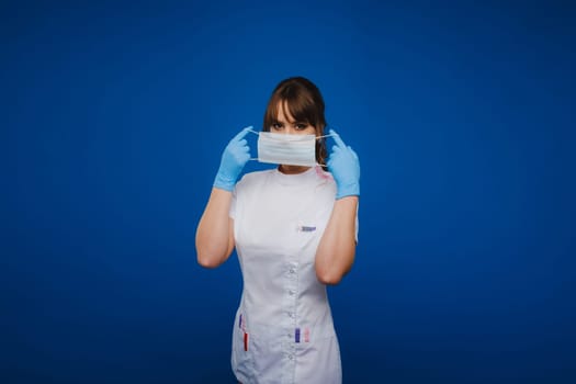 A doctor girl stands in a medical mask on an isolated blue background