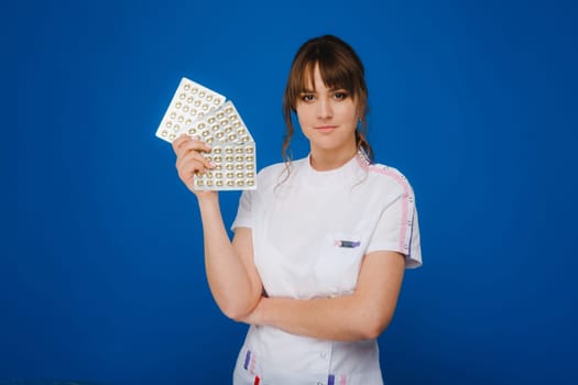 The concept of health care. A young brunette doctor in a white coat on a blue background shows plates with capsules to take