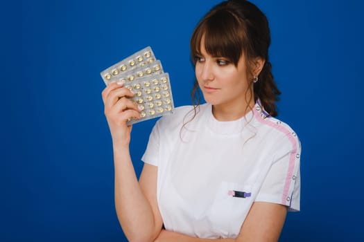 The concept of health care. A young brunette doctor in a white coat on a blue background shows plates with capsules to take