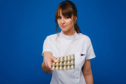 The concept of health care. A young brunette doctor in a white coat on a blue background shows plates with capsules to take