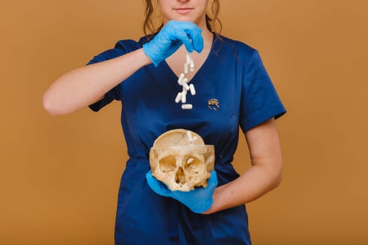 A pretty young doctor pours vitamin capsules into a human skull. The doctor pours pills on the background