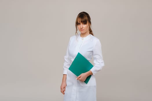 Portrait of a female medical worker in a gray background with a medical report.Girl doctor with a Notepad.