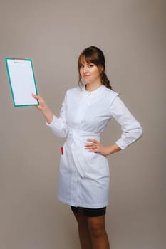 Portrait of a female medical worker in a gray background with a medical report.Girl doctor with a Notepad.