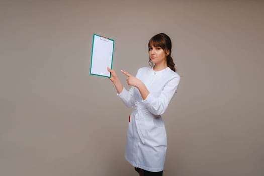 Portrait of a female medical worker in a gray background with a medical report.Girl doctor with a Notepad.