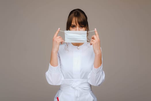 A girl doctor stands in a medical mask, isolated on a gray background