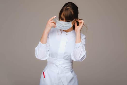 A girl doctor stands in a medical mask, isolated on a gray background