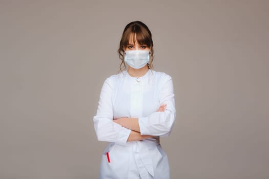 A girl doctor stands in a medical mask, isolated on a gray background