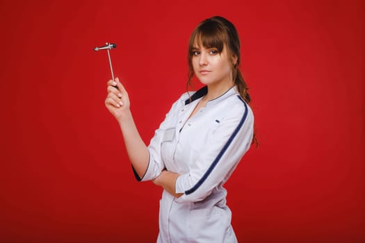 a beautiful doctor girl holds a reflex hammer and smiles at the camera isolated on a Red background.