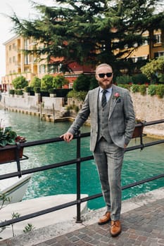 A man with a beard in a strict grey three-piece suit with a tie in the old town of Sirmione, a Stylish man in a grey suit in Italy.