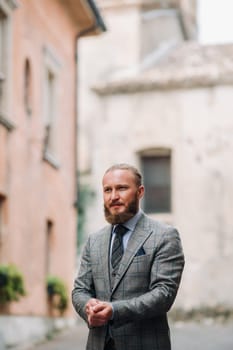 A man with a beard in a strict grey three-piece suit with a tie in the old town of Sirmione, a Stylish man in a grey suit in Italy.